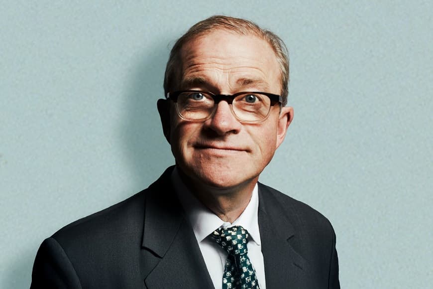 Image of Harry Enfield smirking wearing a suit and tie