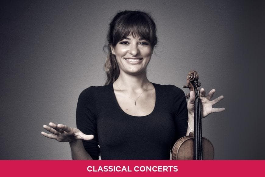 Violinist Nicola Benedetti smiling at the camera holding her violin in her left hand